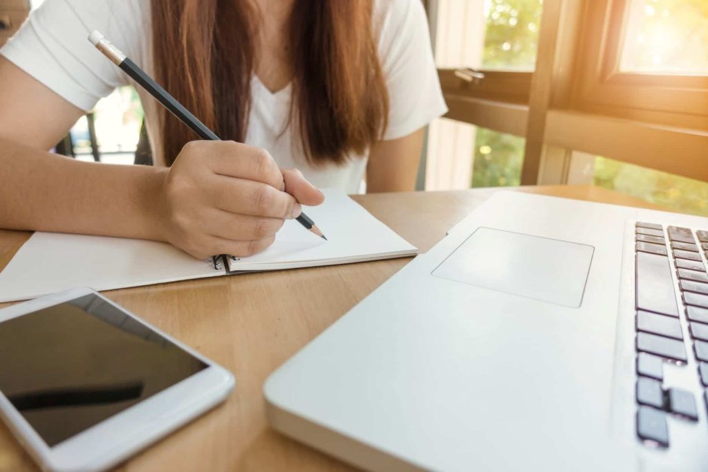 girl writing in notebook by computer