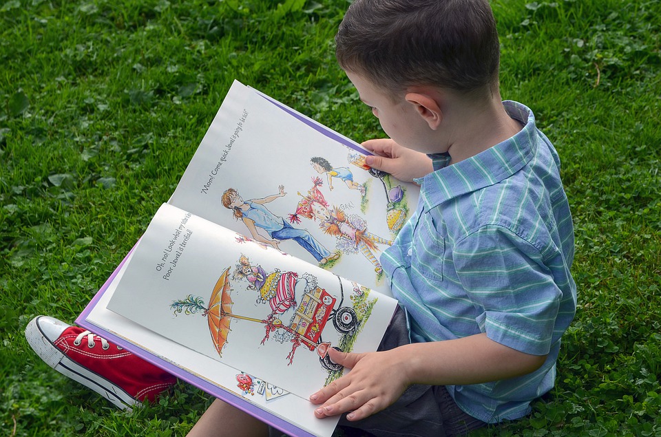 Child reading book on green grass