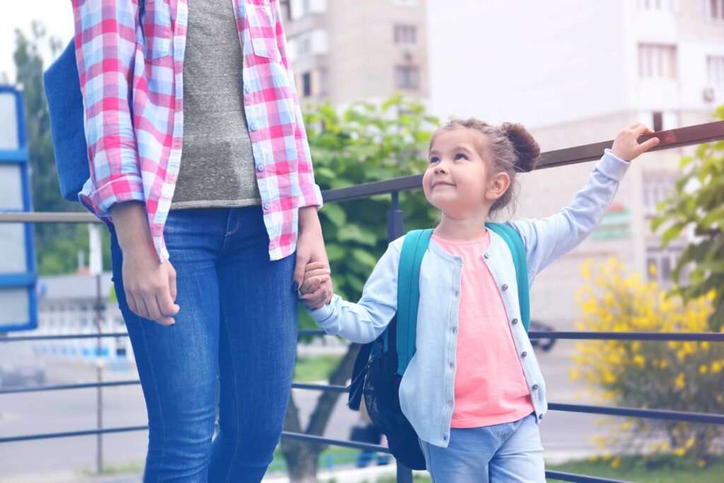 parent and child walking outside holding hands wearing backpacks